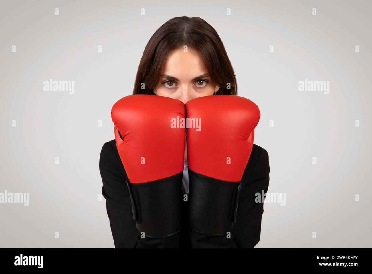 Donna d'affari determinata con uno sguardo mirato che indossa guanti da boxe, simboleggiando l'empowerment Foto Stock