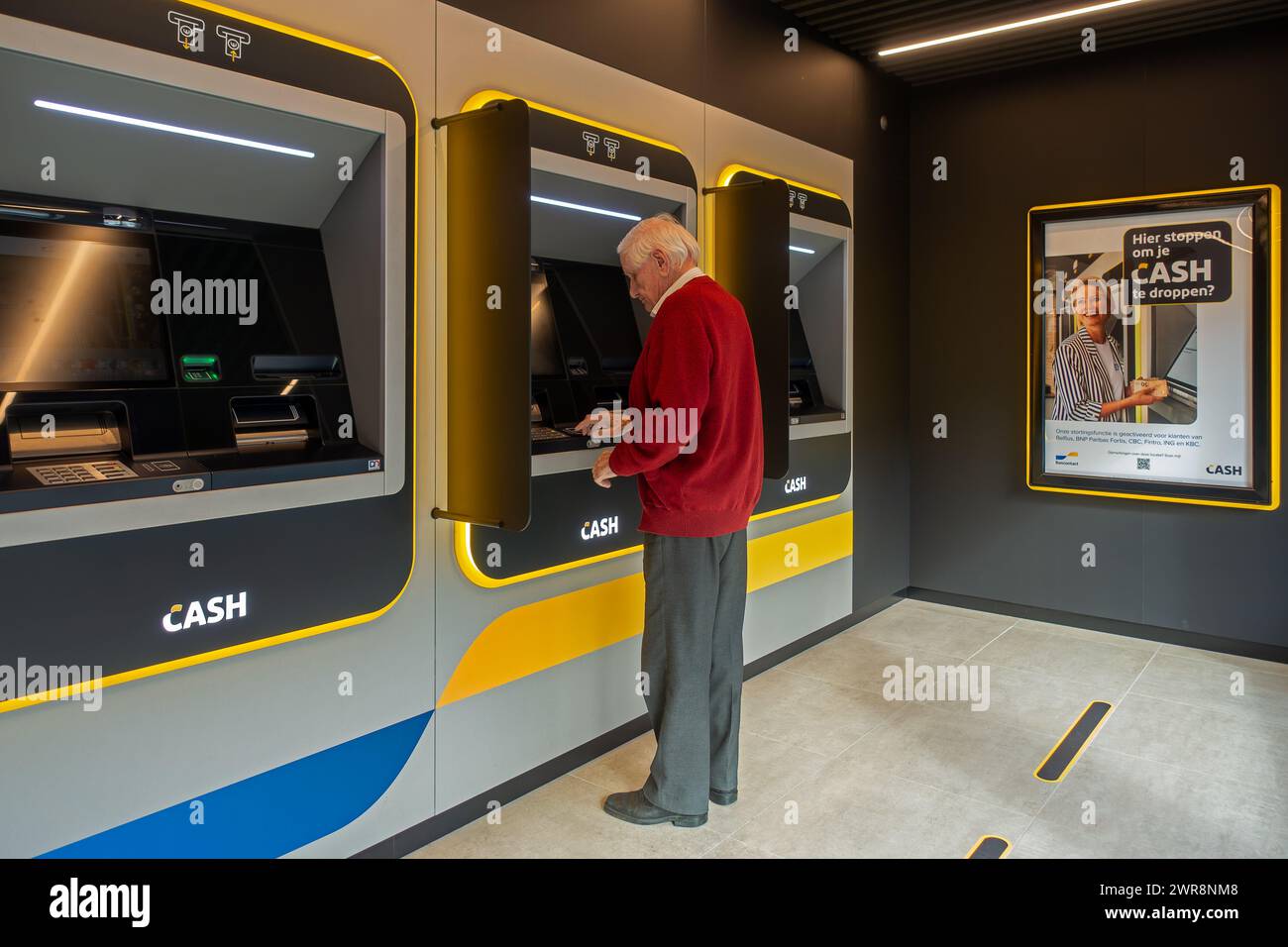 Uomo anziano che raccoglie denaro dal distributore bancomat interno del punto bancomat Bancontact neutrale delle banche nelle Fiandre, Belgio. MODELLO RILASCIATO Foto Stock
