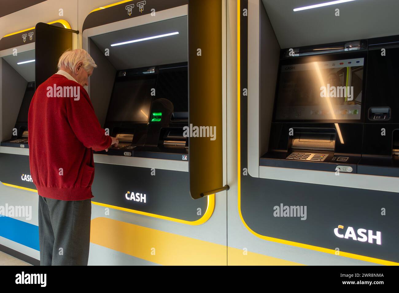 Uomo anziano che raccoglie denaro dal distributore bancomat interno del punto bancomat Bancontact neutrale delle banche nelle Fiandre, Belgio. MODELLO RILASCIATO Foto Stock