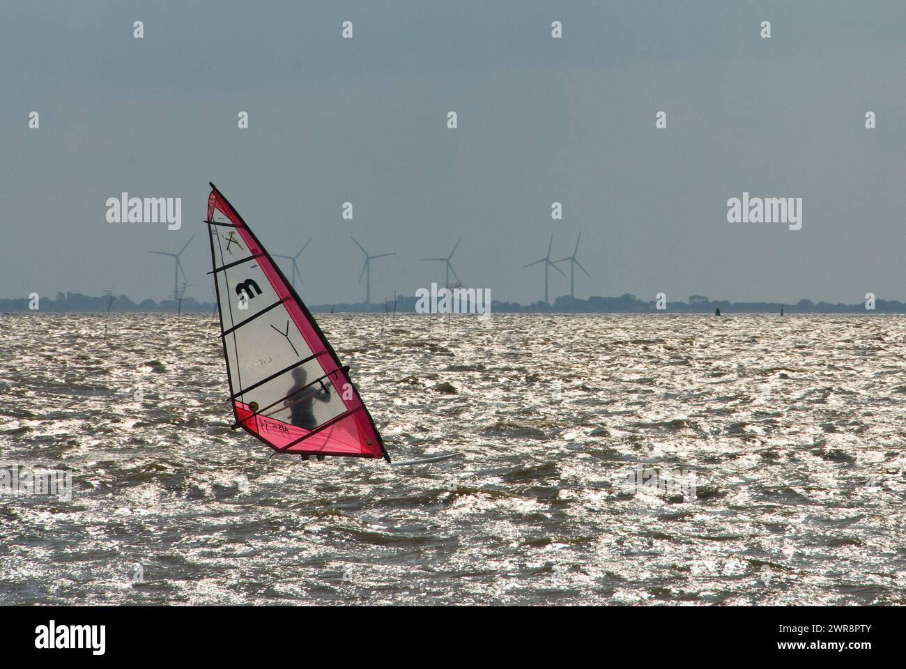 Sailboarder che affronta mari agitati con turbine eoliche lontane Foto Stock