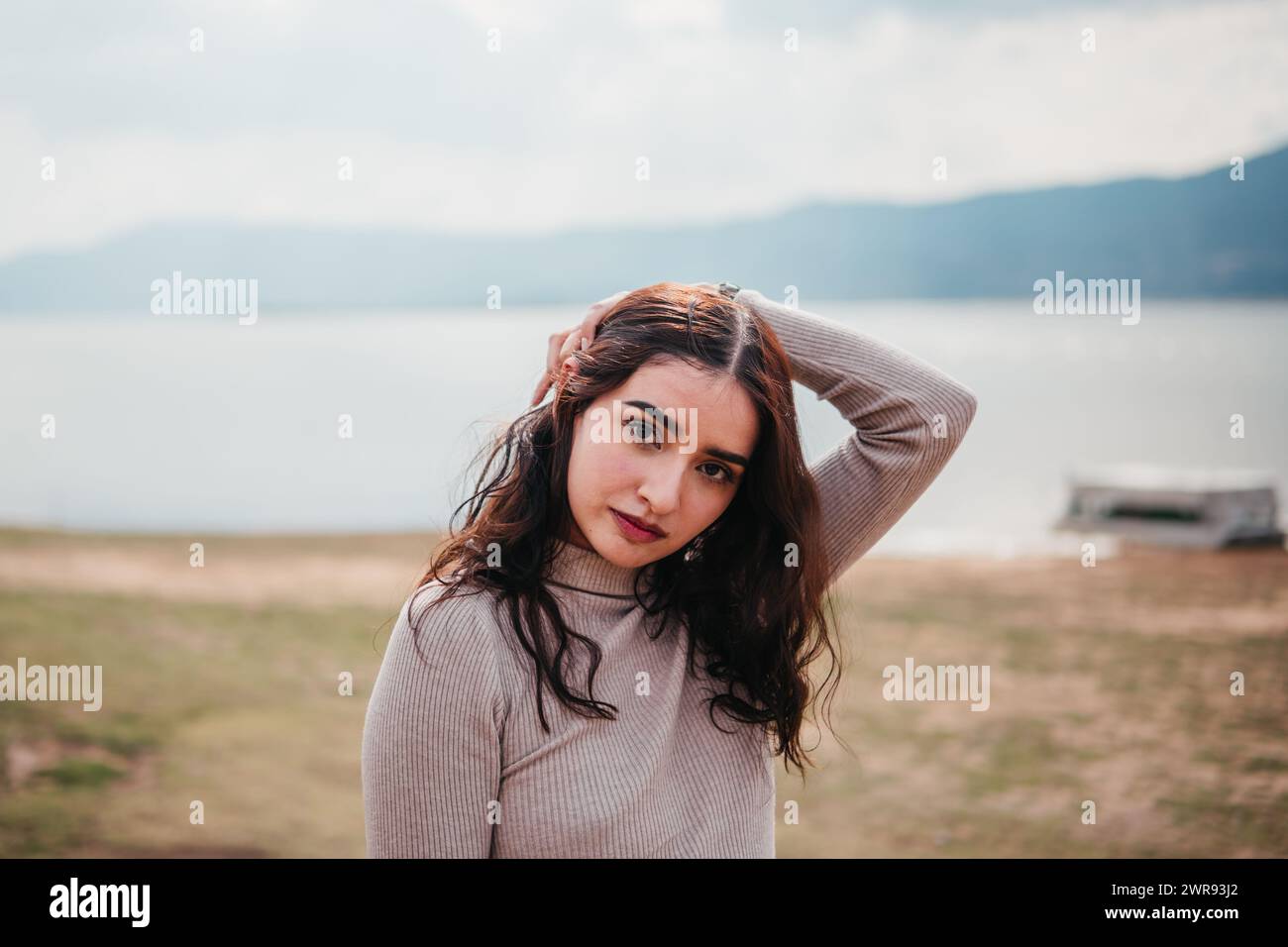 Una donna latina in abbigliamento casual si trova accanto a un lago, dando una posa sottile alla macchina fotografica Foto Stock