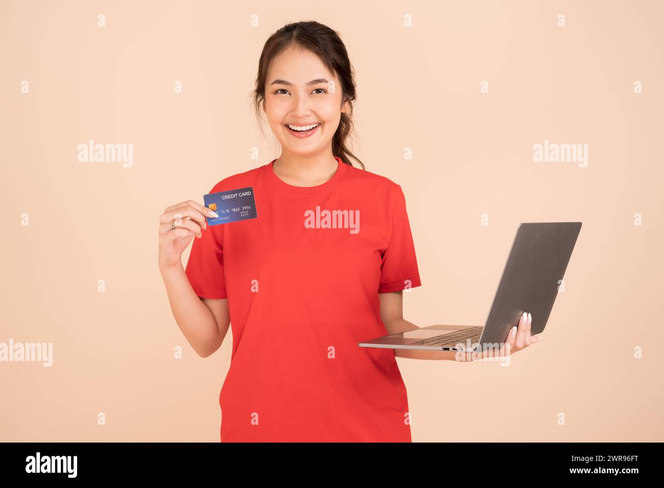 Una giovane donna che indossa una camicia rossa possiede una carta di credito e utilizza un computer portatile per pagare online, acquisti online, e-commerce, banche, Internet café utilizzando il credito Foto Stock