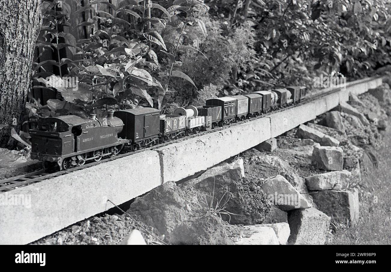 1970, storica, un modello di ferrovia costruito in un giardino sul retro, che mostra il evalato, sopra il binario ferroviario di terra, posizionato su un letto roccioso rialzato, Inghilterra, Regno Unito. Foto Stock