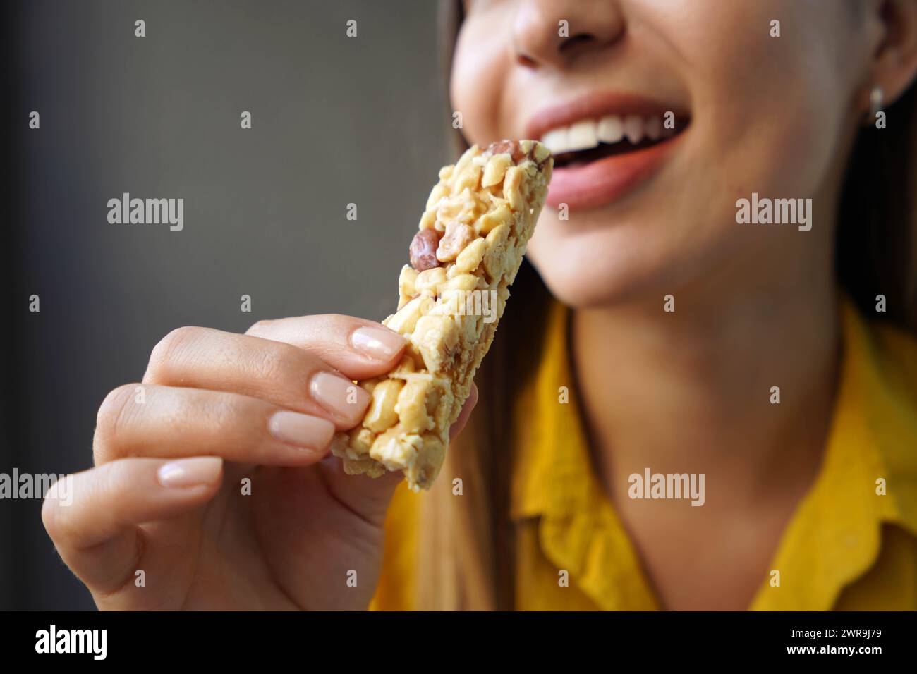 Giovane donna che mangia una barretta di cereali senza zucchero su sfondo grigio Foto Stock