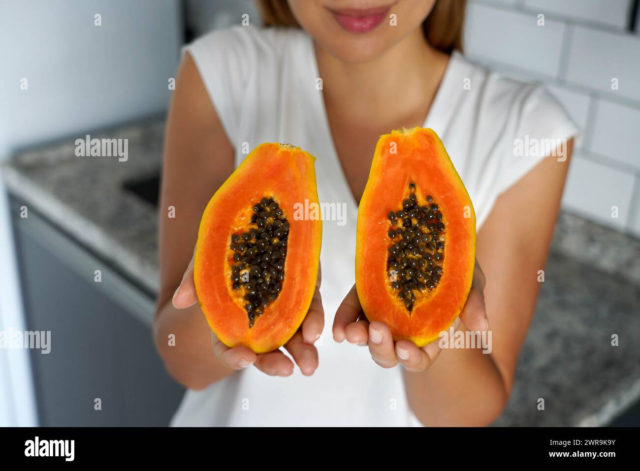 Giovane donna non identificata che mostra una papaya tagliata in due metà in cucina Foto Stock