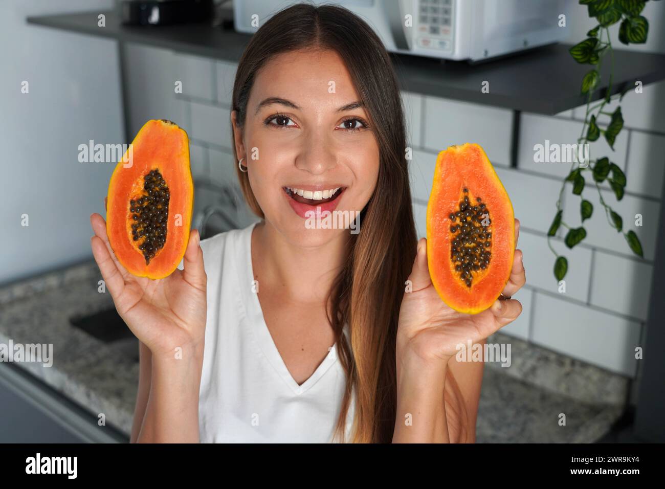 Bella giovane donna che mostra una papaya tagliata in due metà in cucina Foto Stock