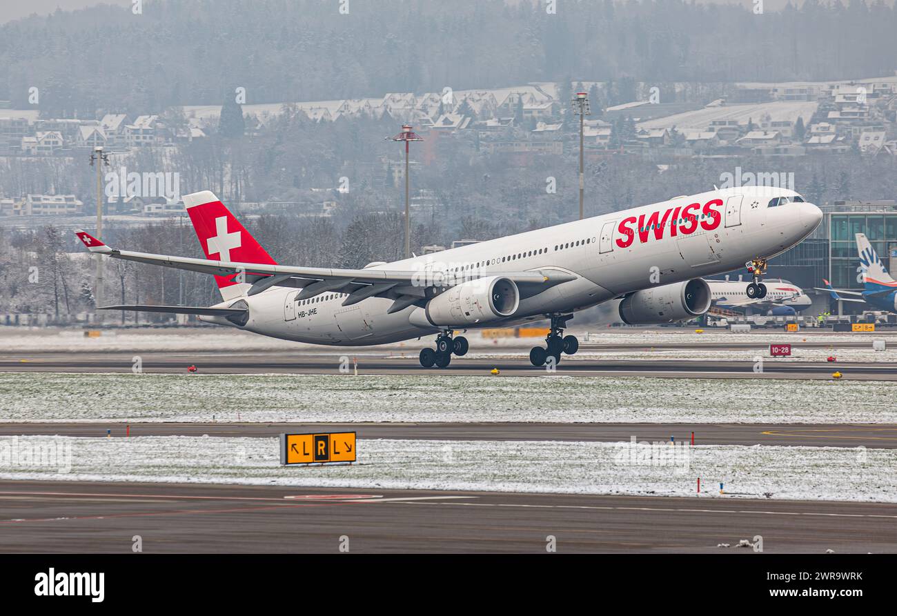 Ein Airbus A330-343X von Swiss International Airlines startet von Startbahn 16 des sich in winterlicher Landschaft befindlichen Flughafen Zürich. Reg Foto Stock