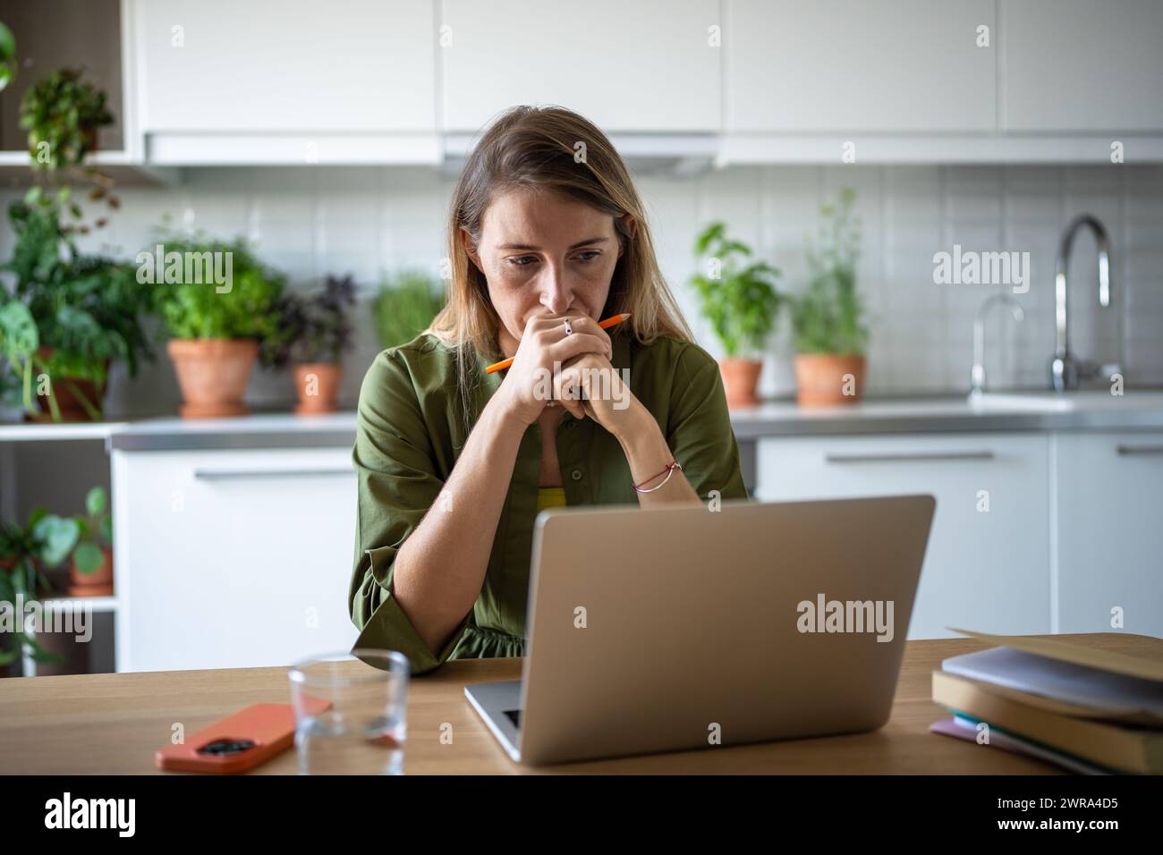 Donna concentrata e premurosa con notebook in profondità nel processo di risoluzione dei problemi relativi alle attività sul campo IT del lavoro remoto. Foto Stock
