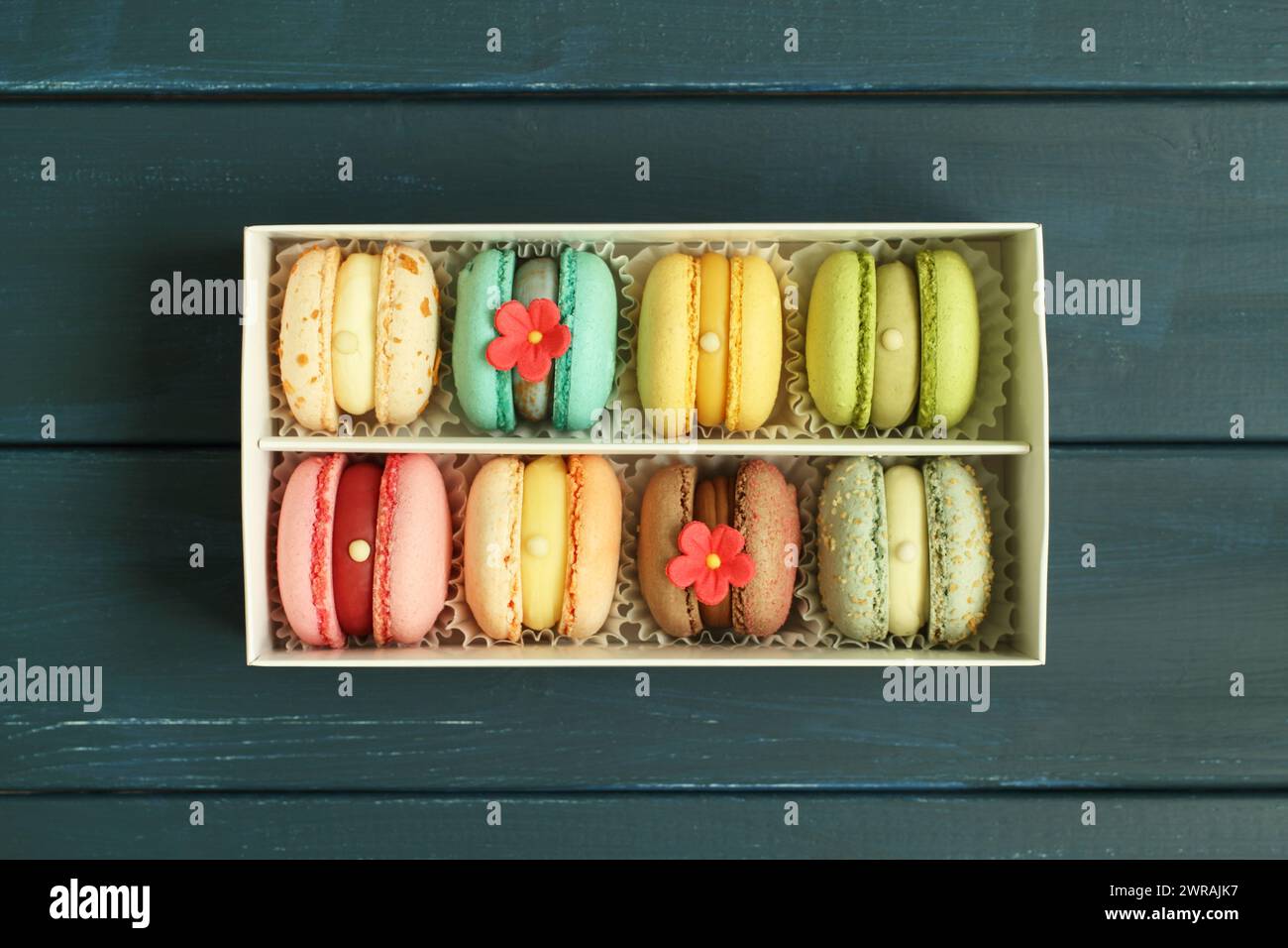 Macaron multicolore in una scatola di cartone bianca su uno sfondo di legno blu. Primo piano. Vista dall'alto verso il basso Foto Stock