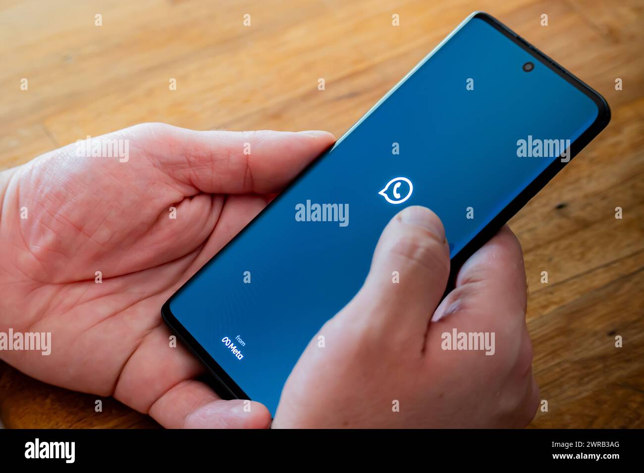 Provincia di Cordoba, Argentina - 11 marzo 2024: Applicazione WhatsApp Meta aperta su un cellulare tenuto dalle mani di un uomo su un tavolo. Foto Stock