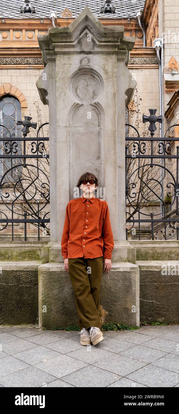 Uomo in stile vintage con occhiali da sole sovradimensionati si erge con sicurezza contro l'edificio storico decorato in un ambiente cittadino. Moderno concetto retrò e nostalgia alla moda. Foto Stock Uomo in stile vintage con occhiali da sole sovradimensionati si erge con sicurezza contro l'edificio storico decorato in un ambiente cittadino. Moderno concetto retrò e nostalgia alla moda. Foto Stock