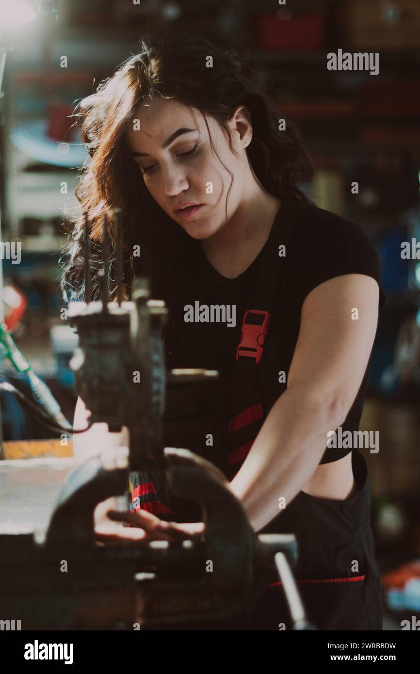 Tecnico donna nel bel mezzo dell'attività di officina, che fissa abilmente un componente con attenzione, un pannello portautensili completo sullo sfondo con effetto bokeh Foto Stock