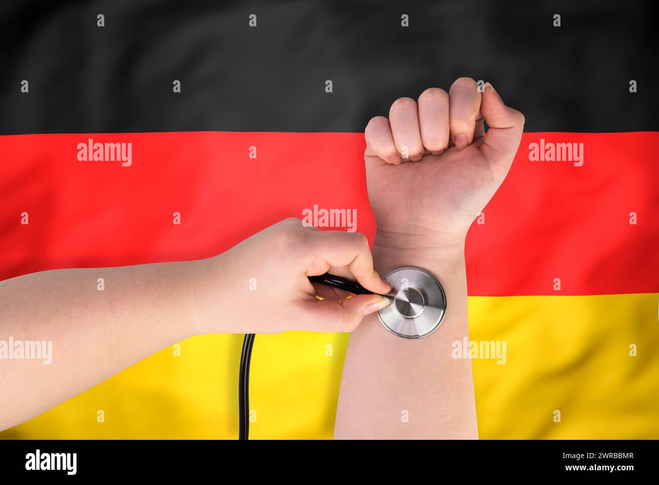 La testa di uno stetoscopio medico sul polso (primo piano) sullo sfondo della bandiera tedesca. Concetto di sistema sanitario tedesco Foto Stock