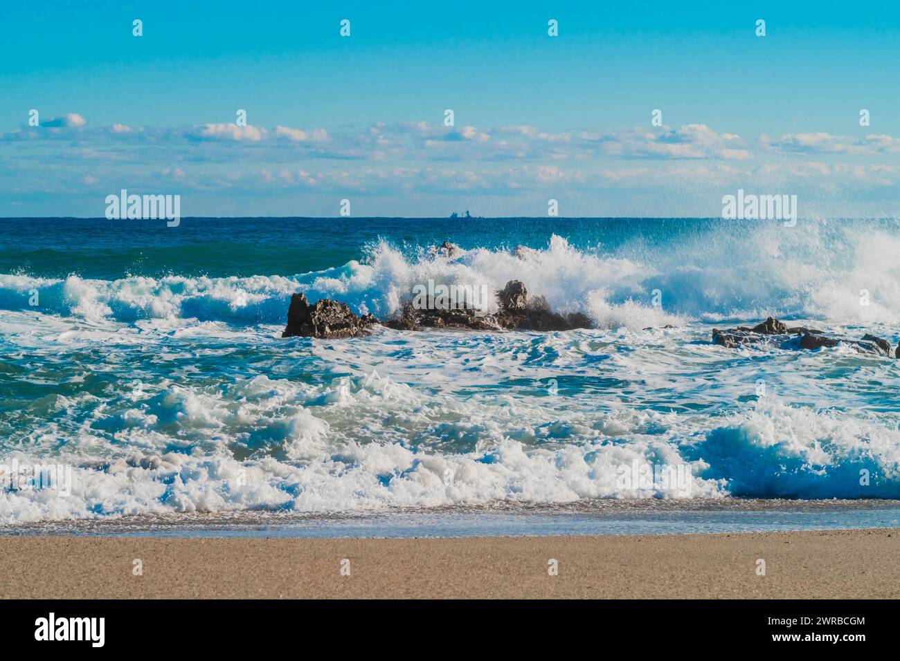 Le onde che si infrangono creano spruzzi intorno alle rocce su una spiaggia soleggiata con orizzonte lontano, in Corea del Sud Foto Stock