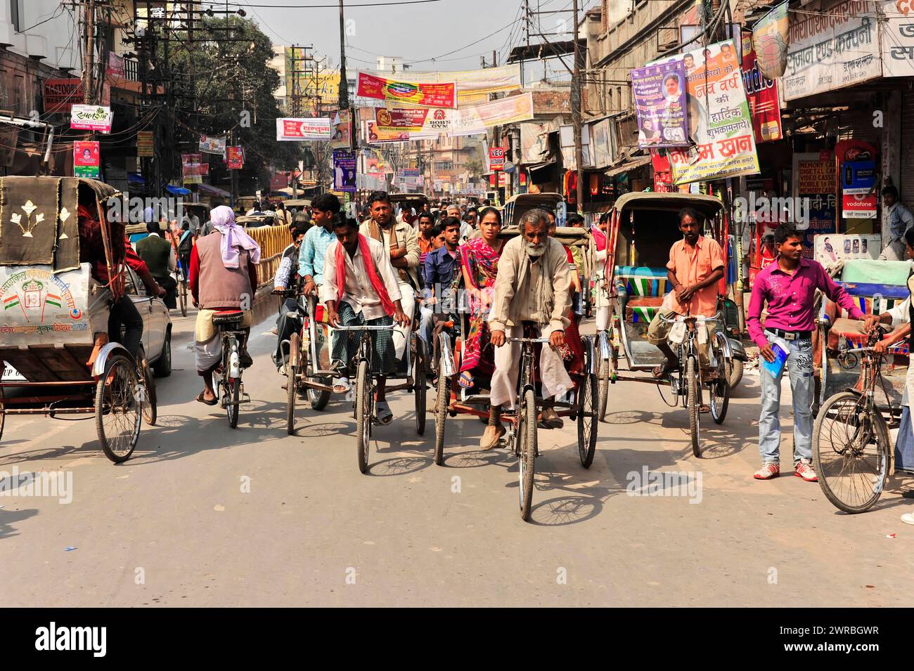 Vivace scena di strada con risciò ciclabili e passanti in una zona trafficata, Varanasi, Uttar Pradesh, India Foto Stock