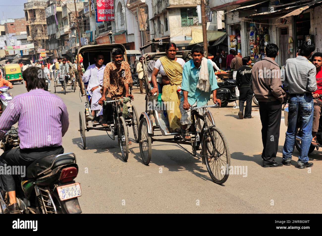 Persone che viaggiano in risciò in una strada trafficata con negozi, Varanasi, Uttar Pradesh, India Foto Stock