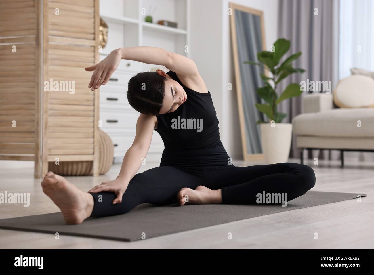 Ragazza che pratica asana con testa a ginocchio ruotata su un tappetino da yoga a casa. Parivrtta janu sirsasana posa Foto Stock