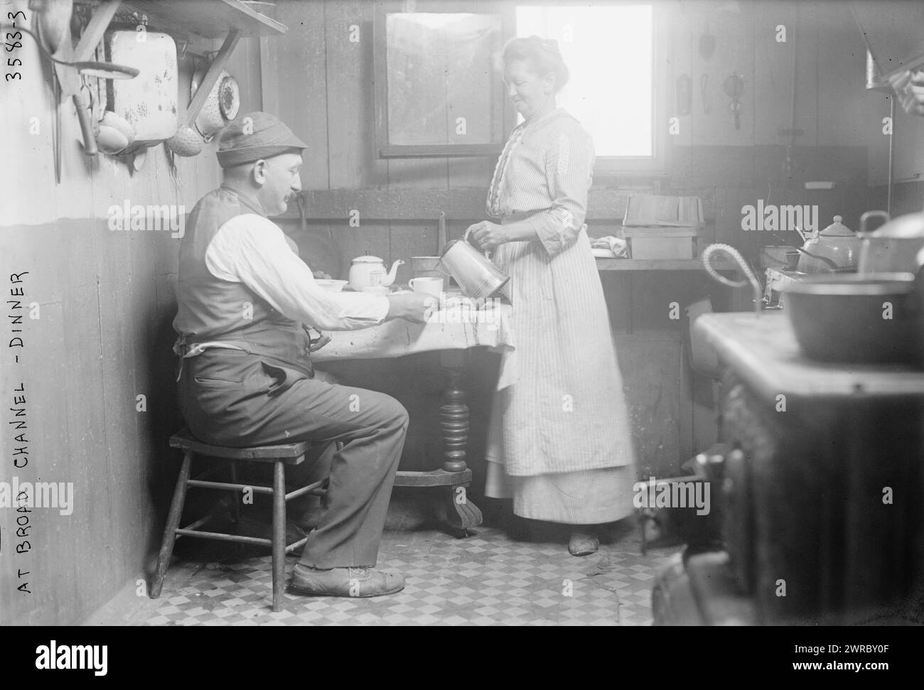A Broad Channel - cena, la fotografia mostra una donna che versa un drink per un uomo seduto a un tavolo in una casa a Broad Channel, Queens, New York City. 1910 e ca. 1915, Glass negative, 1 negativo: Glass Foto Stock