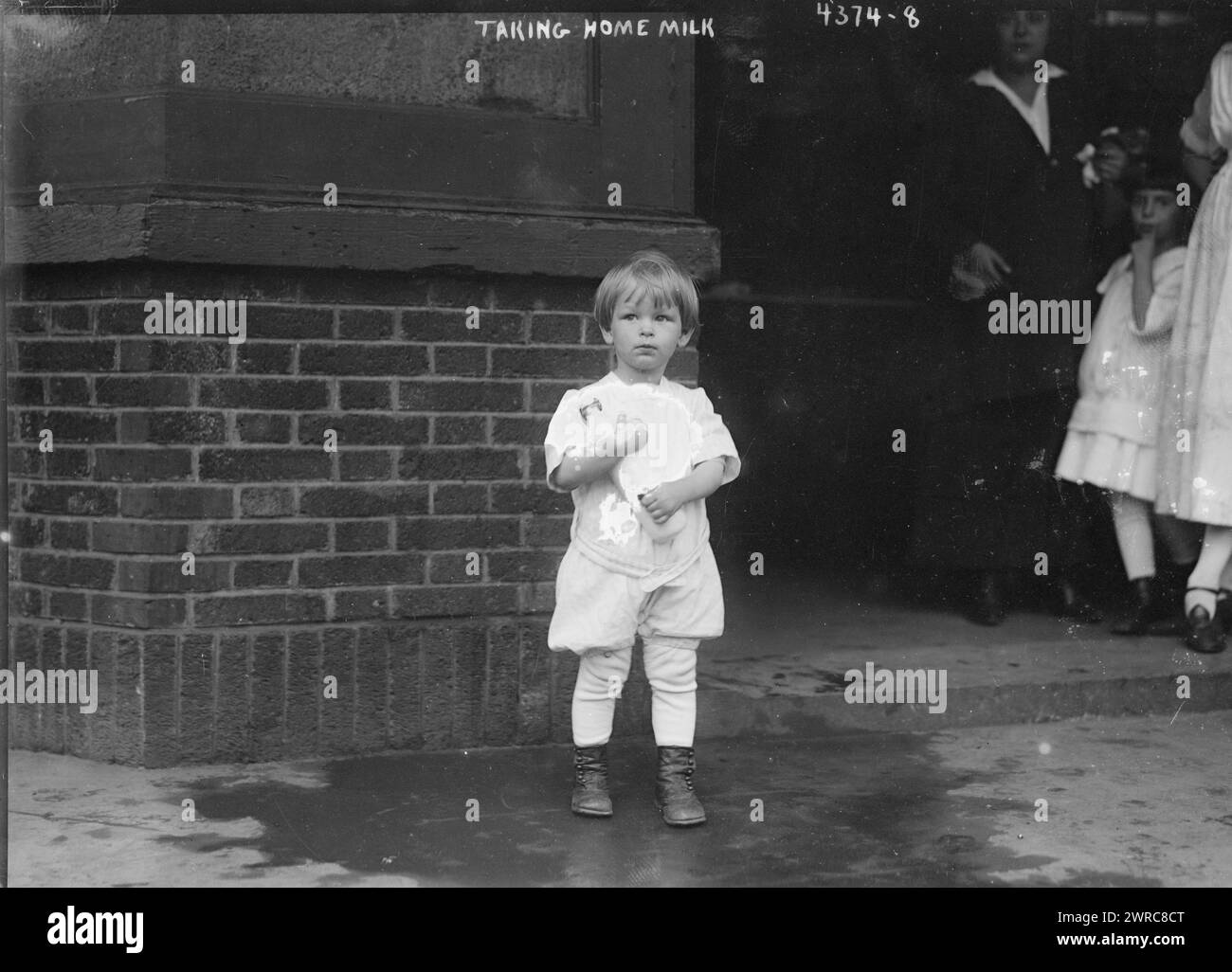 Portando a casa il latte, la fotografia mostra un bambino piccolo che raccoglie il latte in uno dei depositi allestiti dal commerciante Nathan Straus per fornire latte pastorizzato alle famiglie povere. 1915 e ca. 1920, Glass negative, 1 negativo: Glass Foto Stock