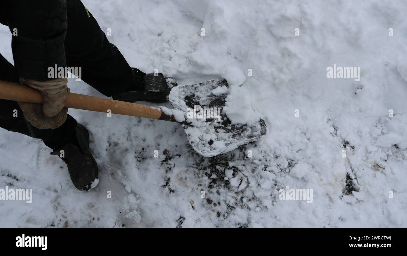 Vista dall'angolo superiore per pulire il grande strato di neve con una pala nelle mani di un uomo con abiti invernali neri, la rimozione di ciaspole Foto Stock