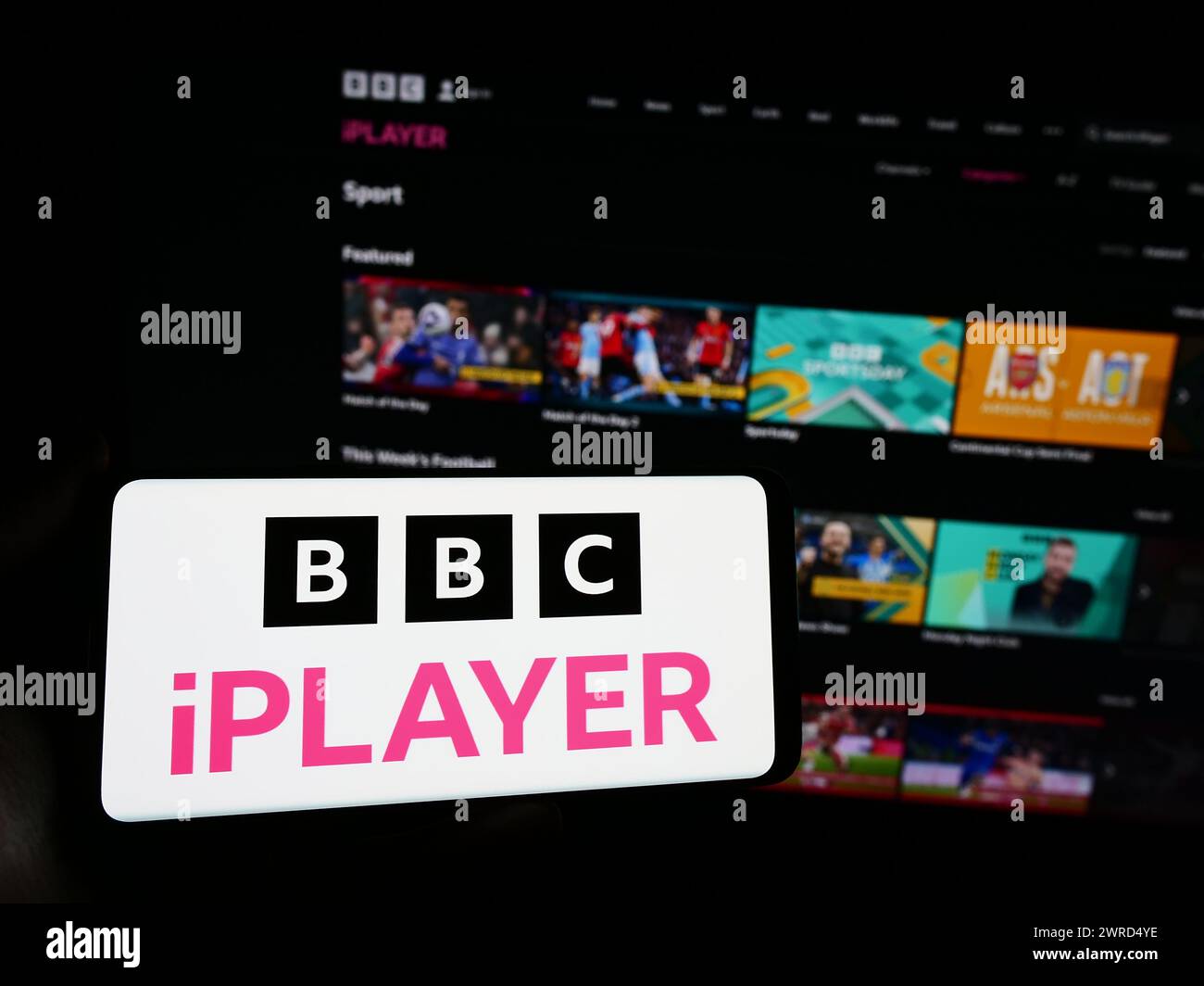 Persona con smartphone con logo del servizio video on demand britannico BBC iPlayer davanti al sito web. Mettere a fuoco il display del telefono. Foto Stock