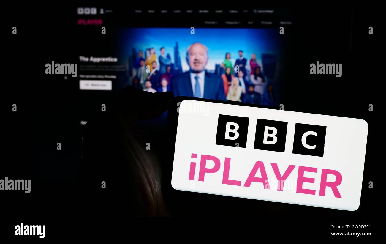 Persona che detiene un telefono cellulare con logo del servizio di video on demand britannico BBC iPlayer davanti alla pagina Web dell'azienda. Mettere a fuoco il display del telefono. Foto Stock