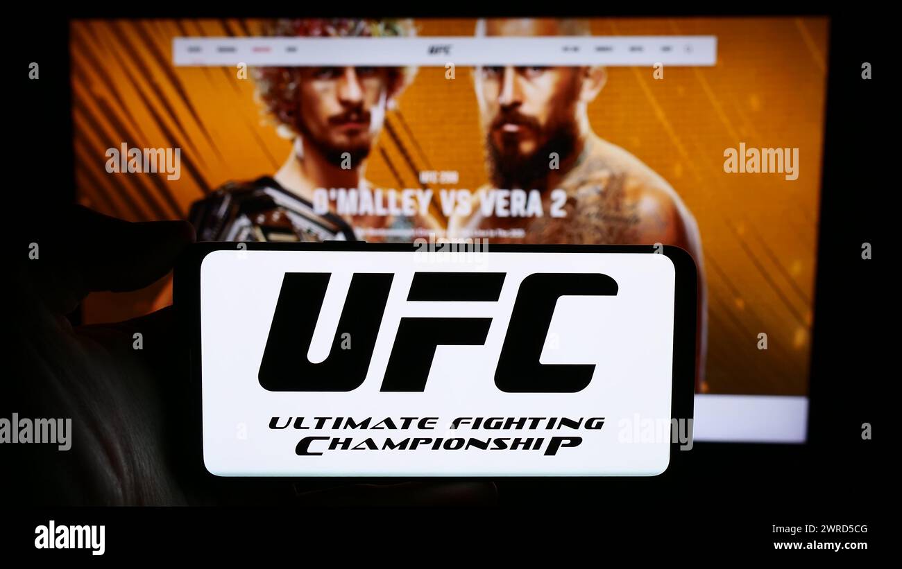 Persona che detiene un cellulare con il logo della società di arti marziali Ultimate Fighting Championship (UFC) davanti alla pagina web. Mettere a fuoco il display del telefono. Foto Stock