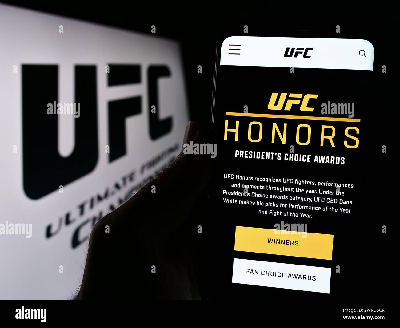 Persona che possiede uno smartphone con pagina web dell'azienda di arti marziali Ultimate Fighting Championship (UFC) con logo. Messa a fuoco al centro del display del telefono. Foto Stock
