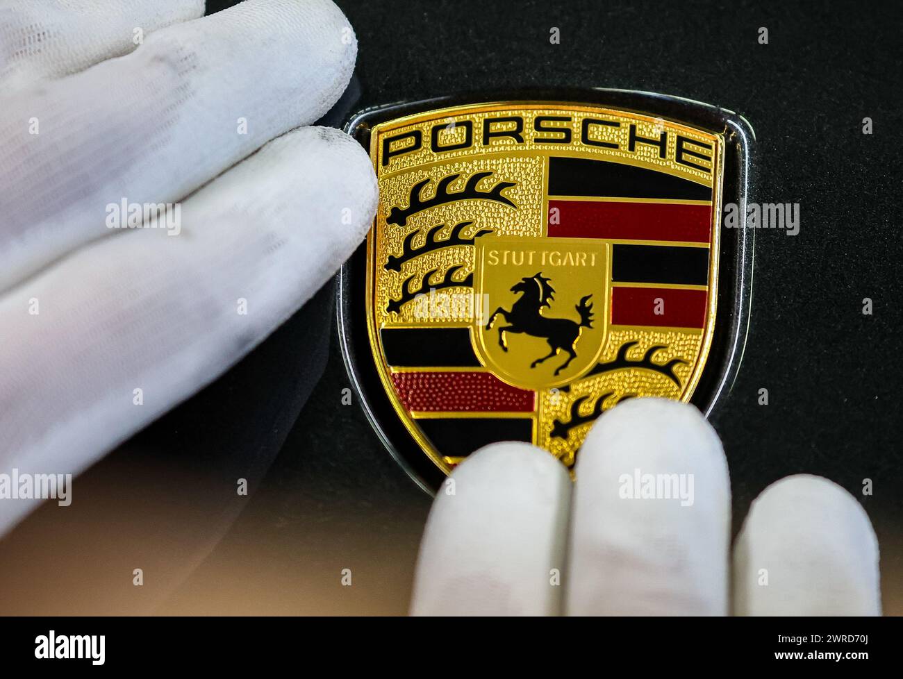 Lipsia, Germania. 11 marzo 2024. Un dipendente attacca il logo del marchio a una Porsche dello stabilimento di Lipsia. Il produttore di veicoli sportivi e fuoristrada Porsche pubblicherà martedì 12 marzo presso lo stabilimento Porsche di Lipsia i dati aziendali relativi all'ultimo anno. Crediti: Jan Woitas/dpa/Alamy Live News Foto Stock