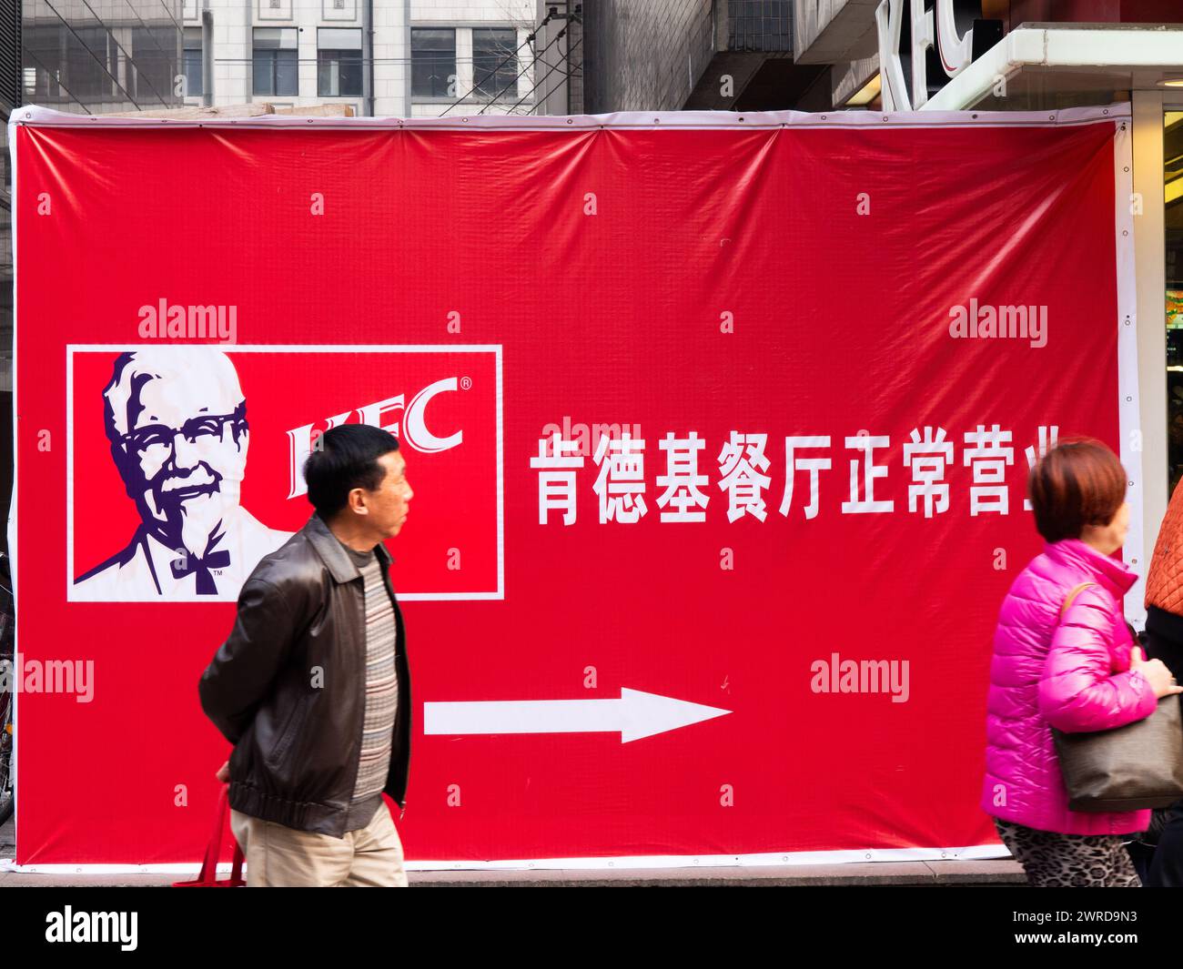 Persone che passano davanti A Un cartello del KFC in cinese con le frecce che puntano, centro città, Shanghai, Cina Foto Stock