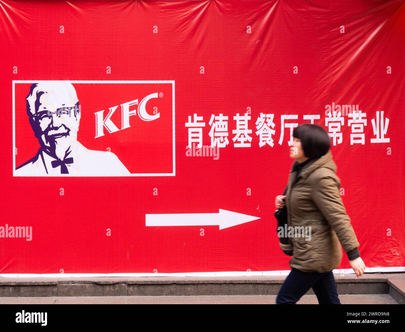 Persone che passano davanti A Un cartello del KFC in cinese con le frecce che puntano, centro città, Shanghai, Cina Foto Stock