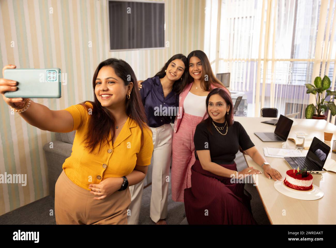 Donna che scatta selfie con i colleghi durante la festa di compleanno in ufficio Foto Stock