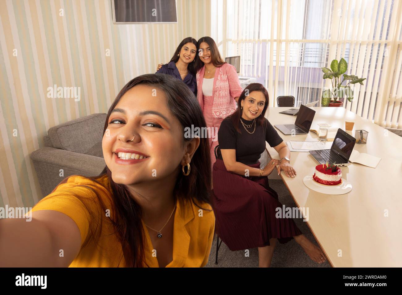 Donna che scatta selfie con i colleghi durante la festa di compleanno in ufficio Foto Stock