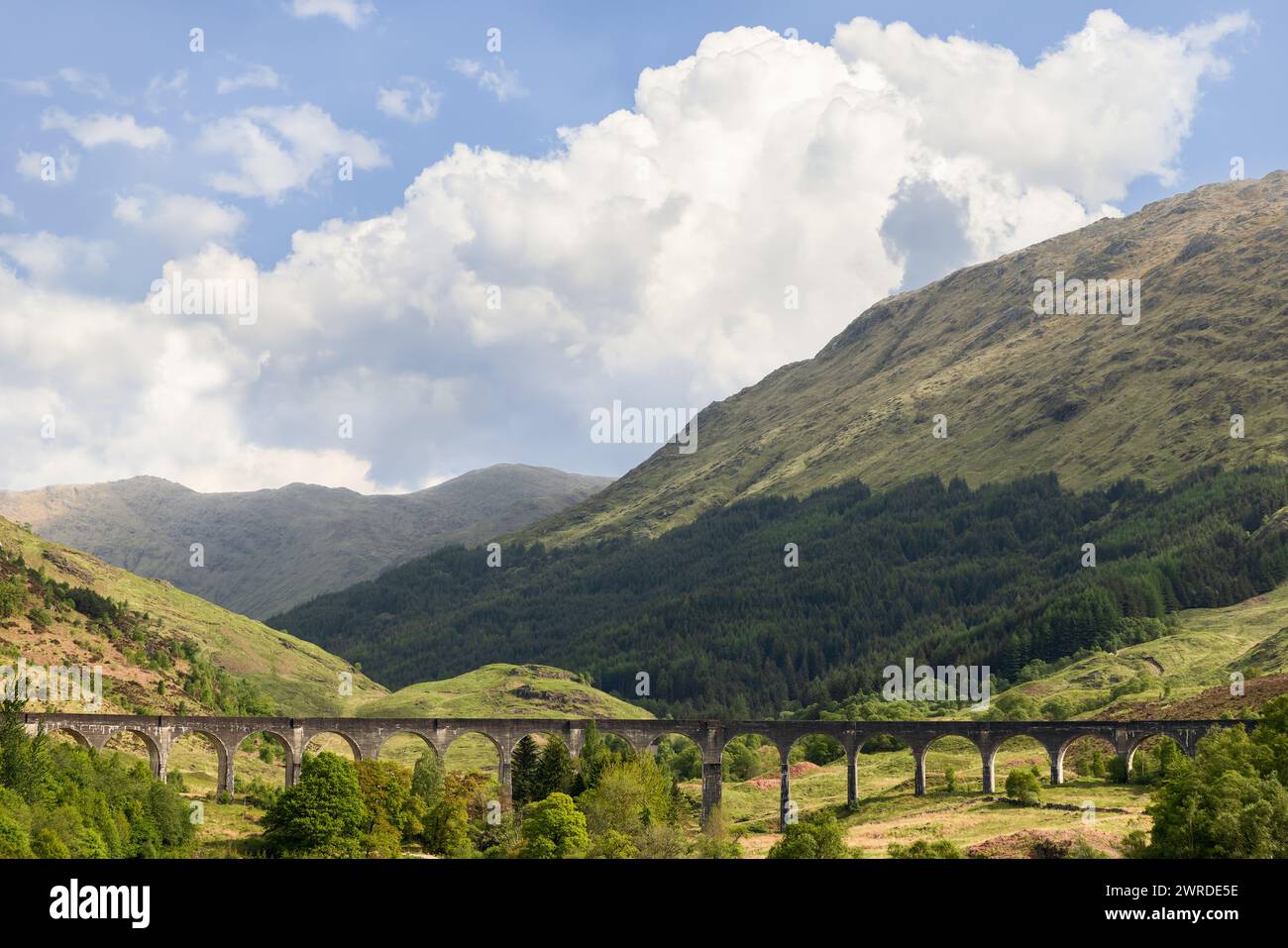 Il viadotto Glenfinnan si snoda attraverso le Highlands scozzesi, con i suoi archi che incorniciano la lussureggiante vegetazione, con terreno montuoso che si innalza sotto un dra Foto Stock