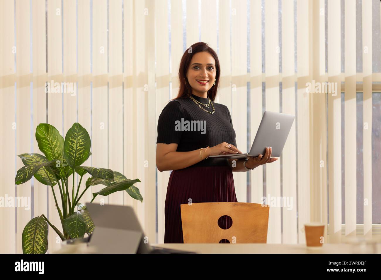 Imprenditrice sorridente con laptop in piedi in ufficio Foto Stock
