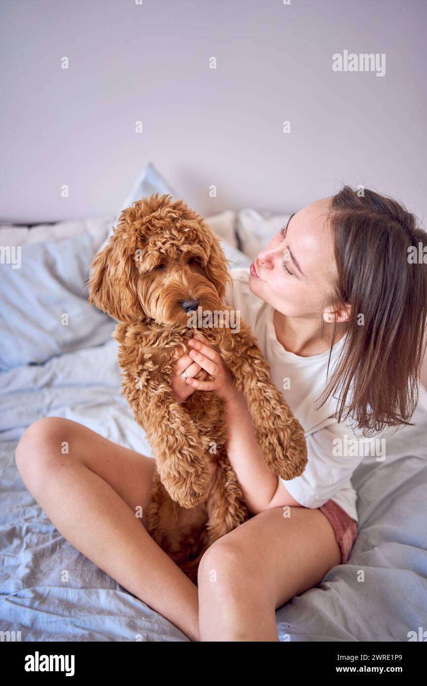 una giovane donna che gioca e bacia una ragazza cockapoo sul letto, minimalismo Foto Stock