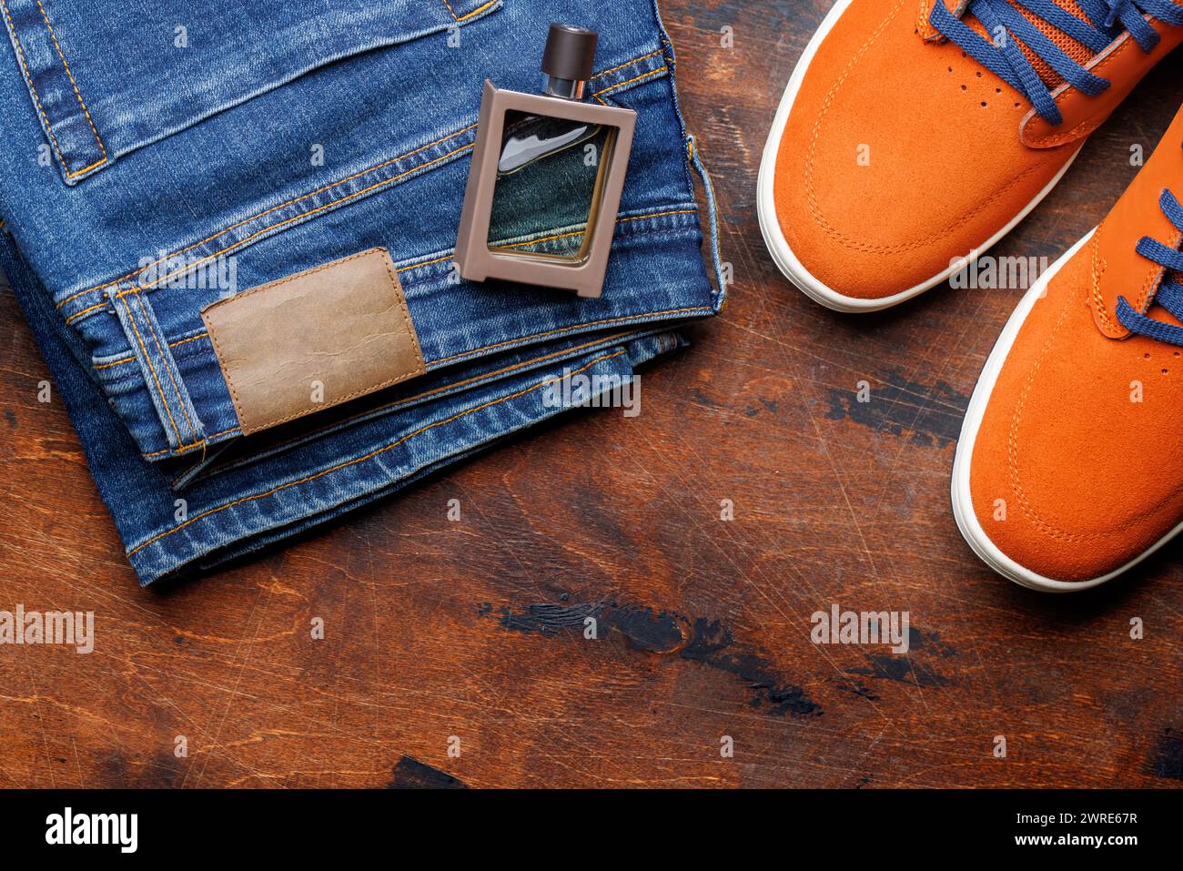 Abbigliamento da uomo su sfondo in legno: Jeans, sneakers, profumo, piatto con spazio copia Foto Stock