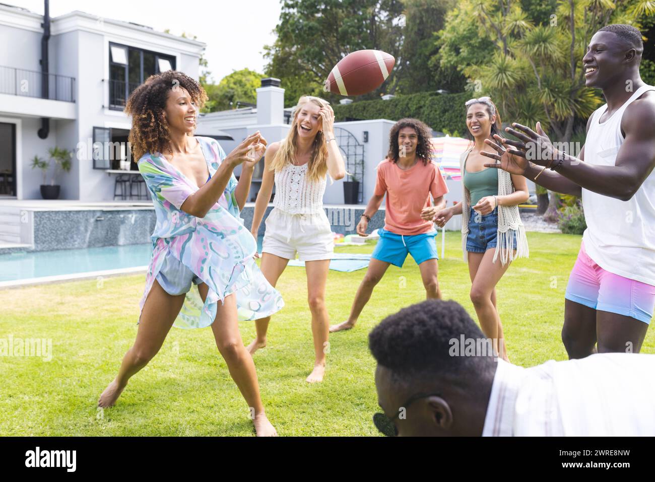 Gruppi diversi di amici si divertono a giocare a calcio in un cortile soleggiato Foto Stock