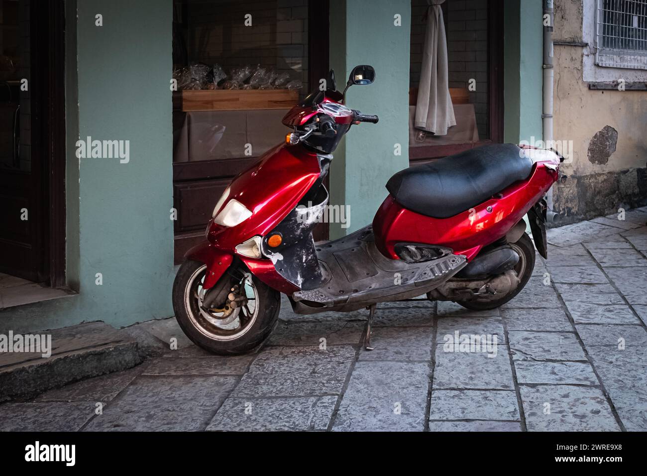 Scooter rosso parcheggiato su un marciapiede nella città vecchia. Scooter uno dei mezzi di trasporto più popolari in Europa. Tipica scena di strada in Grecia con uno scooter outsi Foto Stock