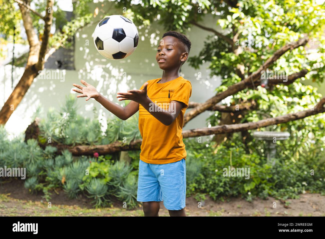 Un ragazzo afroamericano gioca con un pallone da calcio all'aperto in un giardino Foto Stock