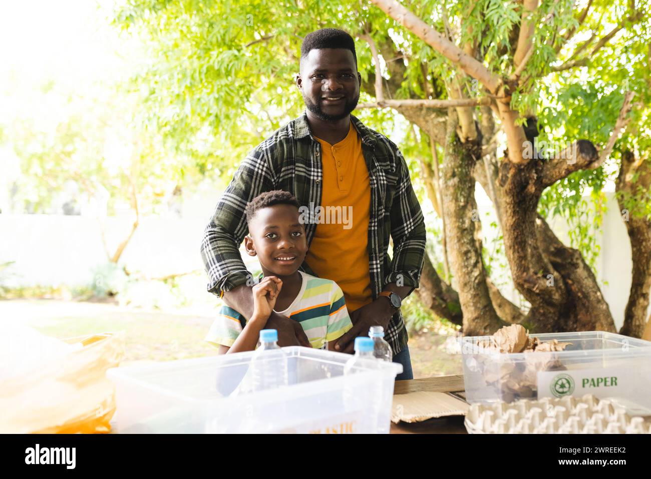 Padre e figlio afroamericani sorridono vicino ai contenitori di riciclaggio all'aperto Foto Stock