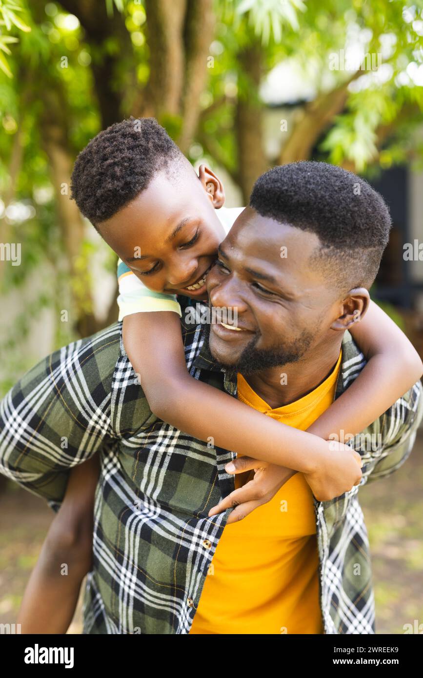 Il padre afroamericano ama fare un giro con suo figlio, entrambi sorridenti in un ambiente all'aperto Foto Stock