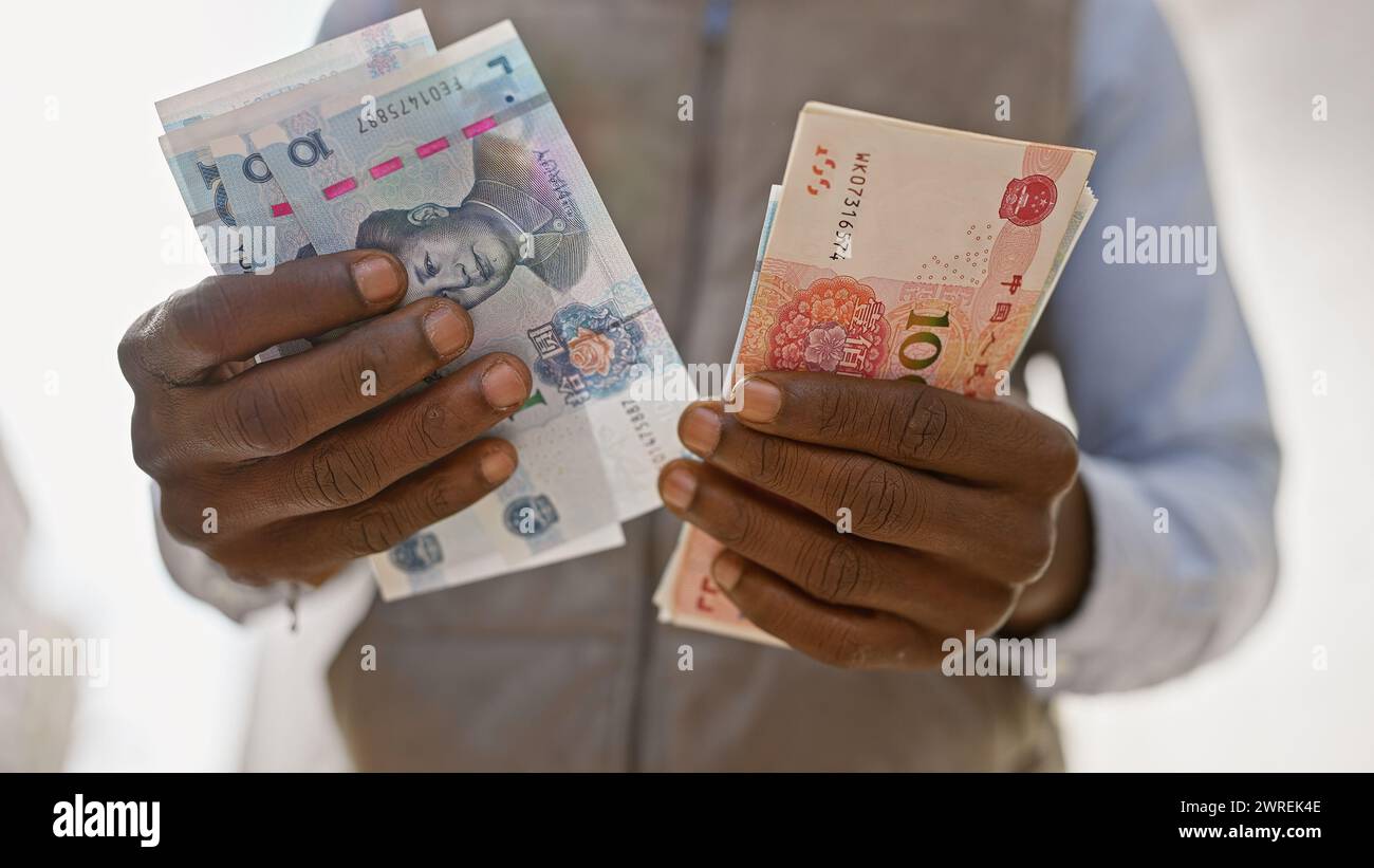 Uomo africano in abbigliamento formale che tiene in mano yuan cinese e valuta estera in una strada urbana. Foto Stock