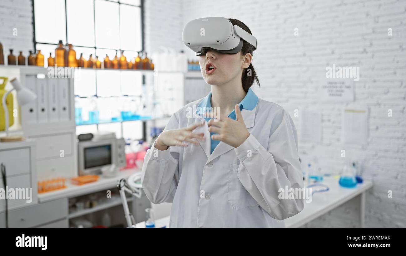 Una giovane scienziata esplora la realtà virtuale in un moderno ambiente di laboratorio, indossando un visore vr tra le attrezzature di laboratorio. Foto Stock