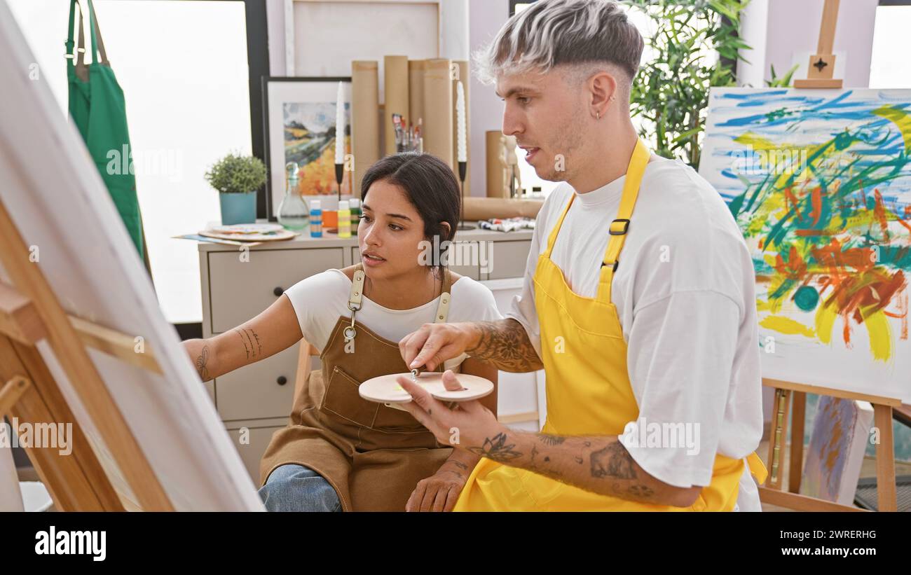 Un uomo e una donna in grembiuli che collaborano a un colorato dipinto astratto in uno studio d'arte. Foto Stock