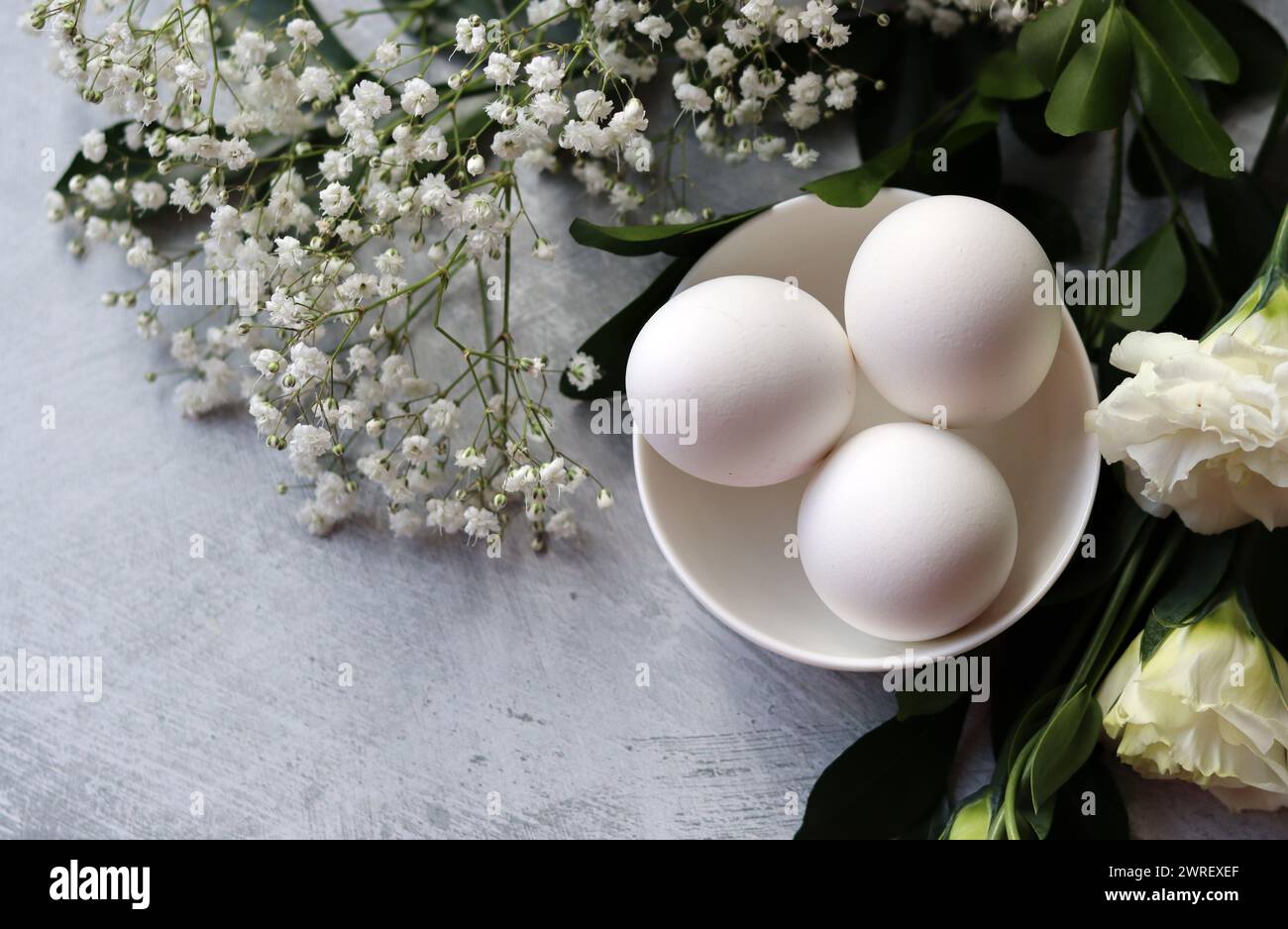 Composizione semplice natura morta con uova e fiori bianchi. Concetto di festa di Pasqua. Uova in un recipiente di ceramica bianco, foto vista dall'alto. Foto Stock