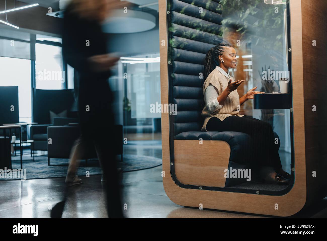 La giovane donna d'affari sorride, seduta in un ufficio di coworking occupato, parla e riesce a fare la sua videochiamata virtuale con altri professionisti. Femmina p Foto Stock