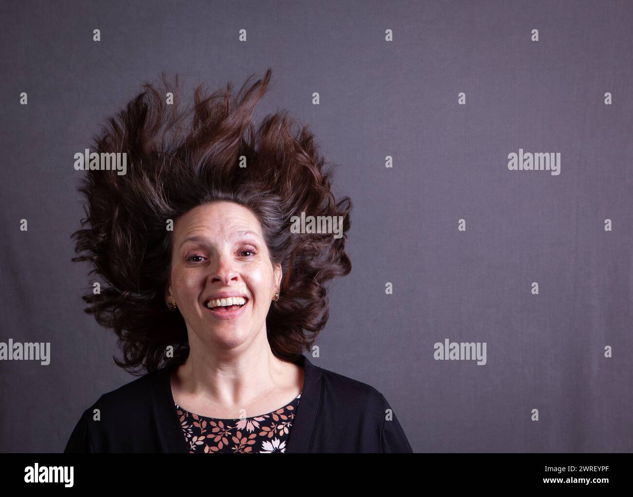 50 qualcosa di donna rilancia i capelli mentre la telecamera blocca il movimento su uno sfondo grigio Foto Stock