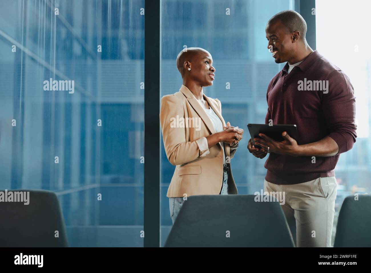 Riunioni aziendali di successo in una sala riunioni aziendale. Un uomo e una donna discutono di idee, usando un tablet. Il loro lavoro di squadra e i loro volti sorridenti ne sono un esempio Foto Stock