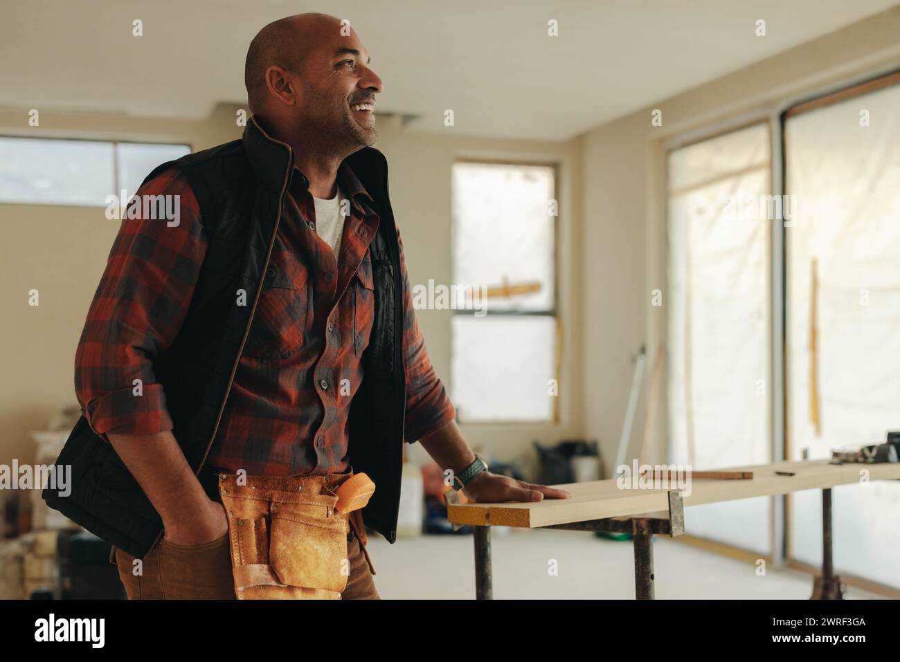 Uomo maturo in una cucina in fase di ristrutturazione. Indossa una cintura portautensili e sorride mentre lavora all'aggiornamento. La sua esperienza nel fai da te lo garantisce Foto Stock